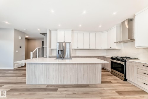 Modern kitchen featuring a large island with an integrated sink, stainless steel appliances, white cabinetry, and light wood flooring - 840 Stillwater Boulevard, Edmonton, AB - Indoor Photo Showing Kitchen With Upgraded Kitchen