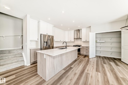 The kitchen features a center island with a sink, white cabinetry, stainless steel appliances, and light wood flooring - 840 Stillwater Boulevard, Edmonton, AB - Indoor Photo Showing Kitchen With Upgraded Kitchen