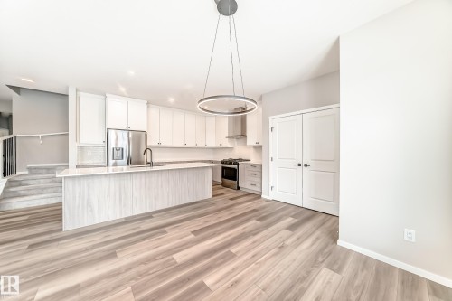 Modern kitchen featuring a large island with a sink and faucet, white cabinetry, stainless steel appliances, and wood-look flooring - 840 Stillwater Boulevard, Edmonton, AB - Indoor Photo Showing Kitchen