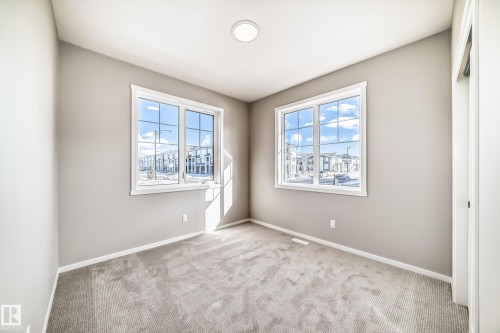 This room features light gray carpeting and two large windows with white trim, allowing for ample natural light - 840 Stillwater Boulevard, Edmonton, AB - Indoor Photo Showing Other Room