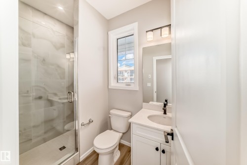 The bathroom features a glass-enclosed shower with tile surround, a single vanity with a white countertop, and a window providing natural light - 840 Stillwater Boulevard, Edmonton, AB - Indoor Photo Showing Bathroom