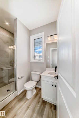 The bathroom features a glass-enclosed shower, a vanity with a white countertop, and wood-look flooring - 840 Stillwater Boulevard, Edmonton, AB - Indoor Photo Showing Bathroom