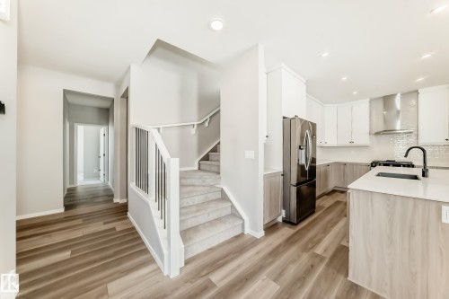 This property features a modern kitchen with a stainless steel refrigerator, white cabinetry, and an island with a sink and a black faucet - 840 Stillwater Boulevard, Edmonton, AB - Indoor Photo Showing Kitchen With Upgraded Kitchen