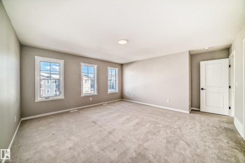 This spacious room features neutral-toned carpeting, three windows providing natural light, and a white interior door with a black handle - 840 Stillwater Boulevard, Edmonton, AB - Indoor Photo Showing Other Room