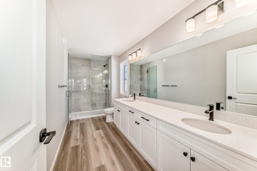 Well-appointed bathroom featuring a double vanity with white cabinetry and quartz countertops, a spacious walk-in shower with glass enclosure, and wood-look flooring - 840 Stillwater Boulevard, Edmonton, AB - Indoor Photo Showing Bathroom