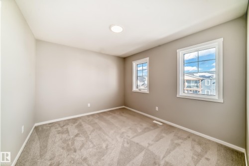 The room features neutral-toned walls, carpeted flooring, and two windows providing natural light - 840 Stillwater Boulevard, Edmonton, AB - Indoor Photo Showing Other Room