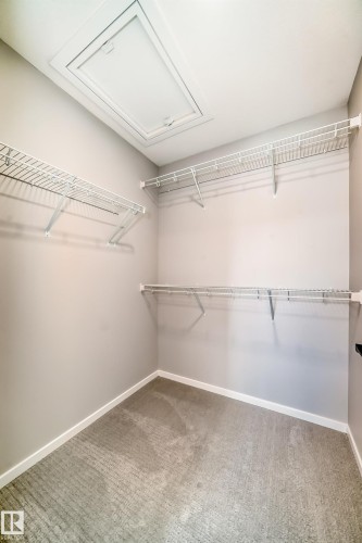 This walk-in closet features carpeted flooring, white wire shelving, and an attic access panel in the ceiling - 840 Stillwater Boulevard, Edmonton, AB - Indoor With Storage