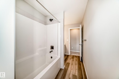 Bathroom featuring a white bathtub and shower combination with dark bronze fixtures, and wood-look flooring - 840 Stillwater Boulevard, Edmonton, AB - Indoor