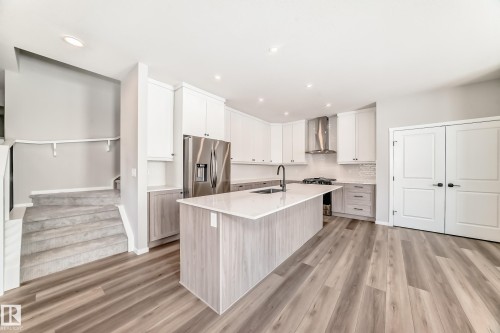 The kitchen features a large island with a sink, white cabinetry, stainless steel appliances, and light-toned flooring - 840 Stillwater Boulevard, Edmonton, AB - Indoor Photo Showing Kitchen