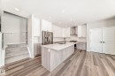 The kitchen features a large island with a sink, white cabinetry, stainless steel appliances, and light-toned flooring - 840 Stillwater Boulevard, Edmonton, AB  - Indoor Photo Showing Kitchen 