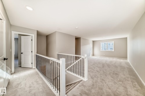 The property features an expansive carpeted area with neutral-toned walls, a staircase with white and black railings, and a window providing natural light - 840 Stillwater Boulevard, Edmonton, AB - Indoor Photo Showing Other Room