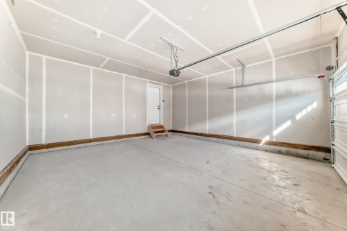 The property features a spacious garage with a concrete floor, a white interior door, and a partially open garage door - 840 Stillwater Boulevard, Edmonton, AB - Indoor Photo Showing Garage