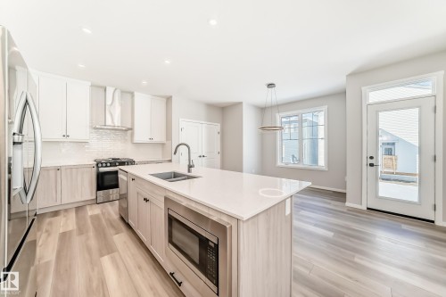 The kitchen features a large island with a sink and built-in microwave, stainless steel appliances, and light-colored cabinetry - 840 Stillwater Boulevard, Edmonton, AB - Indoor Photo Showing Kitchen With Double Sink With Upgraded Kitchen
