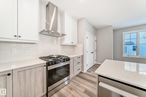 The kitchen features white upper cabinetry, a stainless steel range with a matching range hood, and light-colored countertops - 840 Stillwater Boulevard, Edmonton, AB - Indoor Photo Showing Kitchen With Upgraded Kitchen