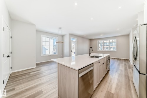 The kitchen features a spacious island with a white countertop and a stainless steel sink, a stainless steel dishwasher, and a stainless steel refrigerator - 840 Stillwater Boulevard, Edmonton, AB - Indoor Photo Showing Kitchen
