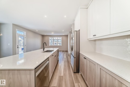 Modern kitchen featuring a large island with a sink and a black faucet, light wood cabinetry, stainless steel appliances, and wood-look flooring - 840 Stillwater Boulevard, Edmonton, AB - Indoor Photo Showing Kitchen With Upgraded Kitchen