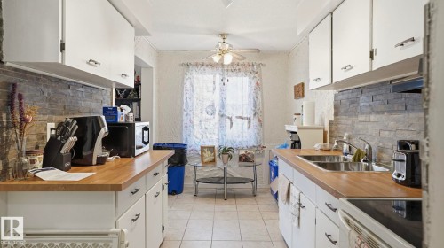 Kitchen featuring white cabinetry, wood-finish countertops, a stacked stone-look backsplash, and a ceiling fan - 12 14120 80 Street, Edmonton, AB - Indoor Photo Showing Kitchen With Double Sink