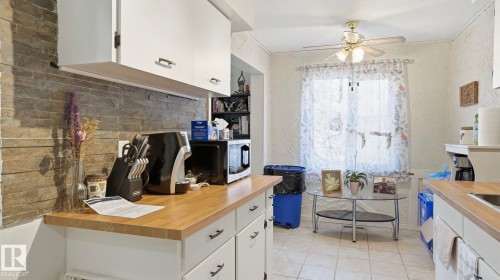 Kitchen featuring butcher block countertops, white cabinetry, a stacked stone backsplash, and ceramic tile flooring - 12 14120 80 Street, Edmonton, AB - Indoor