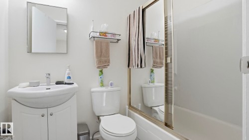 Bathroom featuring a white vanity with integrated sink, chrome faucet, wall-mounted mirror, and a toilet - 12 14120 80 Street, Edmonton, AB - Indoor Photo Showing Bathroom