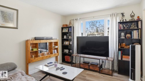 Living area featuring wood-finish flooring, a large window with natural light, and neutral wall paint - 12 14120 80 Street, Edmonton, AB - Indoor Photo Showing Living Room
