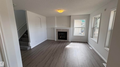The property features a living area with wood-style flooring, a fireplace with a stone surround and white mantel, and windows providing natural light - 10231 163 Street, Edmonton, AB - Indoor Photo Showing Living Room With Fireplace