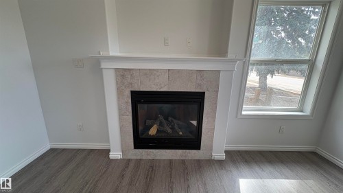 This room features a fireplace with a tiled surround and a mantel, alongside a window providing natural light - 10231 163 Street, Edmonton, AB - Indoor Photo Showing Living Room With Fireplace