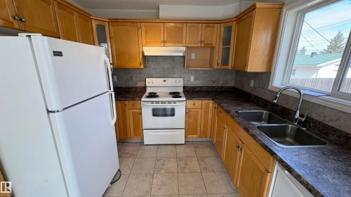 The kitchen features a white refrigerator, a white range, and wood cabinetry - 10231 163 Street, Edmonton, AB - Indoor Photo Showing Kitchen With Double Sink