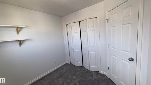 This room features neutral-toned carpet, white walls, and a white six-panel door with a silver knob - 10231 163 Street, Edmonton, AB - Indoor Photo Showing Other Room