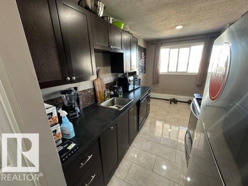 Kitchen featuring dark wood cabinetry, a stainless steel sink, a dark countertop, and a tiled backsplash - 86 13435 97 Street, Edmonton, AB - Indoor Photo Showing Kitchen