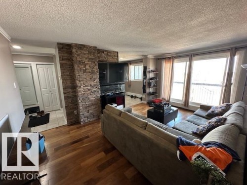 Living area featuring wood-finish flooring, a stacked stone accent wall, and multiple large windows - 86 13435 97 Street, Edmonton, AB - Indoor Photo Showing Living Room