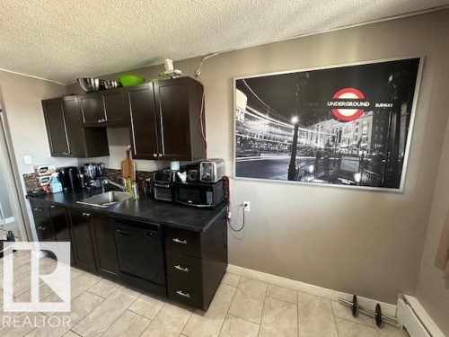 Kitchen featuring dark wood-finish cabinetry, a stainless steel sink, a black dishwasher, and black countertops - 86 13435 97 Street, Edmonton, AB - Indoor Photo Showing Kitchen With Double Sink