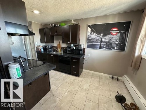 Kitchen featuring dark wood cabinetry, black countertops, stainless steel range hood, and tile flooring - 86 13435 97 Street, Edmonton, AB - Indoor Photo Showing Kitchen