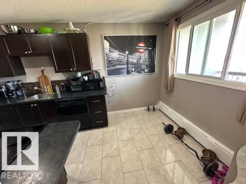 Kitchen featuring dark wood-finish cabinetry, black countertop, tile backsplash, and stainless steel sink - 86 13435 97 Street, Edmonton, AB - Indoor