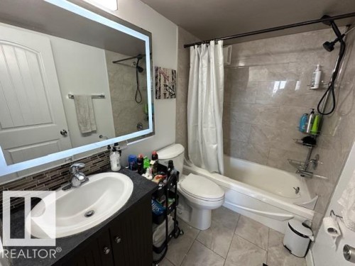 Contemporary bathroom featuring an illuminated vanity mirror, dark wood-finish cabinetry, tiled backsplash, and a tub-shower combination with gray wall tiling and a flexible showerhead - 86 13435 97 Street, Edmonton, AB - Indoor Photo Showing Bathroom