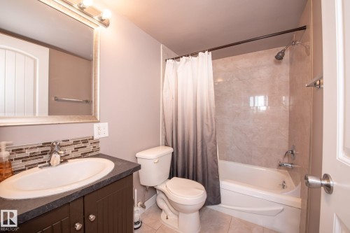 Bathroom with a built-in tub-shower combination, tiled shower surround, and a vanity featuring a vessel sink with a mosaic tile backsplash - 86 13435 97 Street, Edmonton, AB - Indoor Photo Showing Bathroom