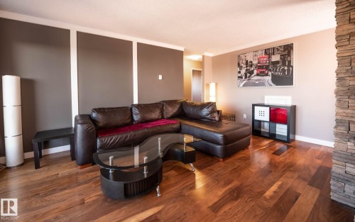 Living area featuring wide plank wood-finish flooring, a stacked stone accent column, and modern wall paneling - 86 13435 97 Street, Edmonton, AB - Indoor Photo Showing Living Room