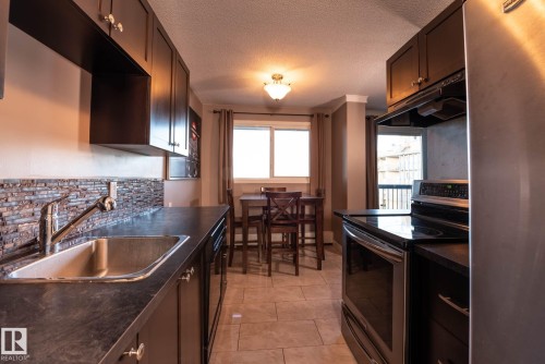 Modern kitchen featuring dark wood cabinetry, stainless steel appliances, a textured tile backsplash, and durable stone-finish countertops - 86 13435 97 Street, Edmonton, AB - Indoor Photo Showing Kitchen