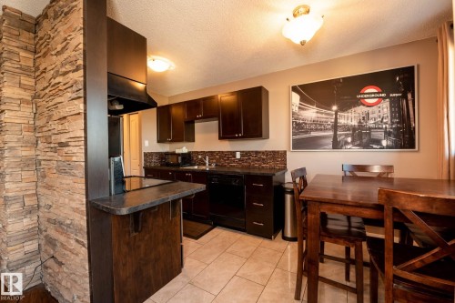 Kitchen featuring dark cabinetry, a built-in cooktop, and a stone-finish accent wall - 86 13435 97 Street, Edmonton, AB - Indoor