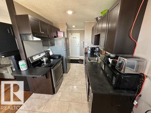 Kitchen featuring dark wood-finish cabinetry, stainless steel appliances, dark countertops, and tile flooring - 86 13435 97 Street, Edmonton, AB - Indoor Photo Showing Kitchen