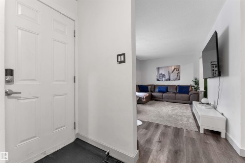 Entryway featuring a paneled door with modern hardware, leading to a living area with wood-finish flooring - 7 14115 82 Street, Edmonton, AB - Indoor Photo Showing Other Room