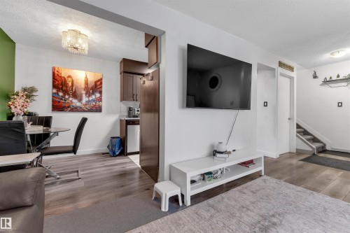 Open-concept living area featuring wood-finish flooring, a contemporary ceiling light fixture, a dedicated dining space with a glass-top table, and a kitchen area with dark wood cabinetry - 7 14115 82 Street, Edmonton, AB - Indoor