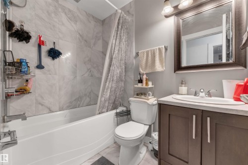 Bathroom featuring a white tub, shower with marble-look tile surround, dark wood-finish vanity with countertop, and framed mirror with integrated lighting - 7 14115 82 Street, Edmonton, AB - Indoor Photo Showing Bathroom
