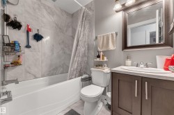 Bathroom featuring a white tub, shower with marble-look tile surround, dark wood-finish vanity with countertop, and framed mirror with integrated lighting - 