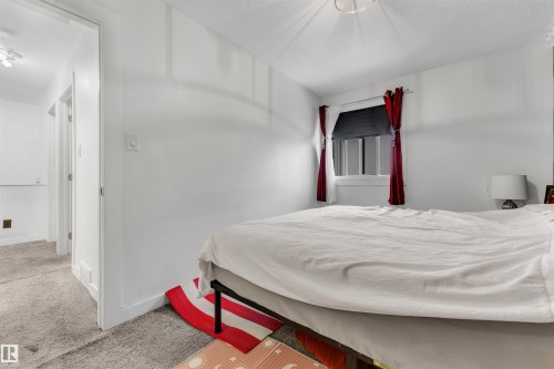 Carpeted bedroom featuring a single window with white trim, a textured ceiling, and a doorway opening to a carpeted hallway - 7 14115 82 Street, Edmonton, AB - Indoor Photo Showing Bedroom