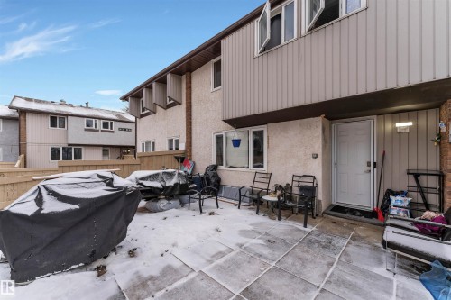Rear exterior featuring a patio with large square pavers, a white paneled door, and multiple white-framed windows - 7 14115 82 Street, Edmonton, AB - Outdoor With Exterior