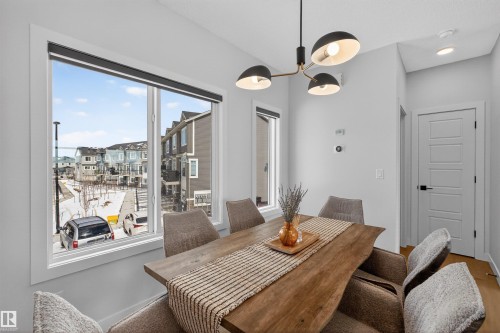 The dining area features a large window, providing natural light, and a modern chandelier - 28 6214 Cartmell Crest, Edmonton, AB - Indoor