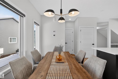 Dining area featuring a modern chandelier, a wooden dining table, and light gray walls - 28 6214 Cartmell Crest, Edmonton, AB - Indoor Photo Showing Dining Room