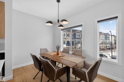 Dining area featuring light hardwood flooring, a modern light fixture, and two large windows providing natural light - 28 6214 Cartmell Crest, Edmonton, AB - Indoor Photo Showing Dining Room