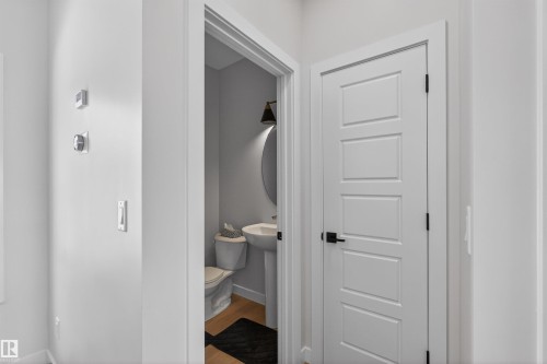 The property features a powder room with a pedestal sink, toilet, and an oval mirror, complemented by an overhead wall sconce - 28 6214 Cartmell Crest, Edmonton, AB - Indoor Photo Showing Other Room