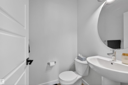 The bathroom features a modern toilet, a pedestal sink with a contemporary faucet, and a round wall-mounted mirror - 28 6214 Cartmell Crest, Edmonton, AB - Indoor Photo Showing Bathroom